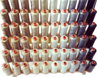 May include: A wooden spool rack with multiple spools of thread in various colors, including beige, white, gray, and black.