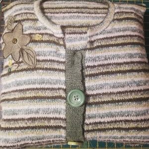 Puede incluir: Una funda de almohada a rayas hecha de un su&eacute;ter reutilizado con un bot&oacute;n verde y un adorno floral.
