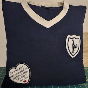 Puede incluir: Una almohada azul marino con cuello en V blanco y un escudo bordado blanco con un p&aacute;jaro. La almohada tiene un parche en forma de coraz&oacute;n con el texto "This is the shirt I used to wear, when you hold it know I am there Love Dad".