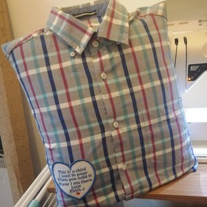 Puede incluir: Una almohada con forma de camisa a cuadros gris, azul y rojo con un parche bordado en forma de coraz&oacute;n que dice "This is a shirt I used to wear When you hold it Know I am there. Love Keith."