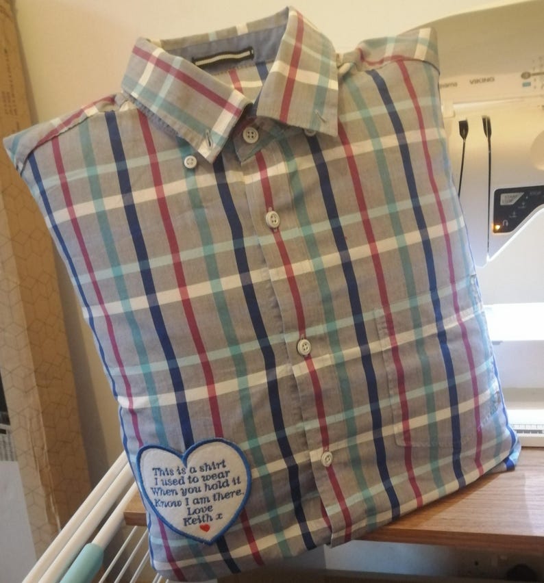 Puede incluir: Una almohada con forma de camisa a cuadros gris, azul y rojo con un parche bordado en forma de coraz&oacute;n que dice "This is a shirt I used to wear When you hold it Know I am there. Love Keith."