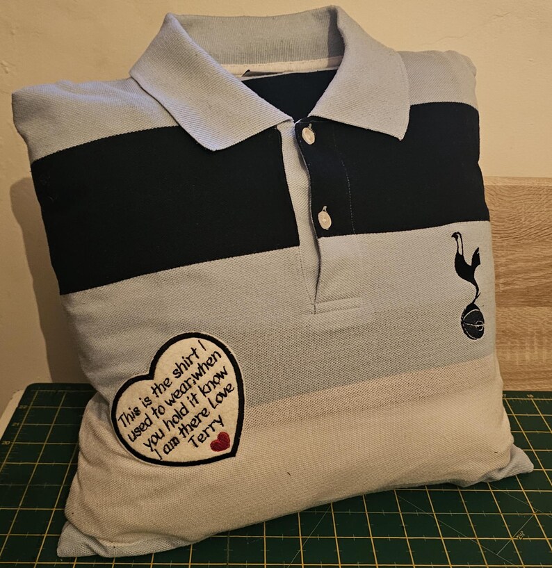 Puede incluir: Una almohada a rayas azules y negras con un coraz&oacute;n bordado blanco que dice "This is the shirt I used to wear, when you hold it know I am there Love Terry".