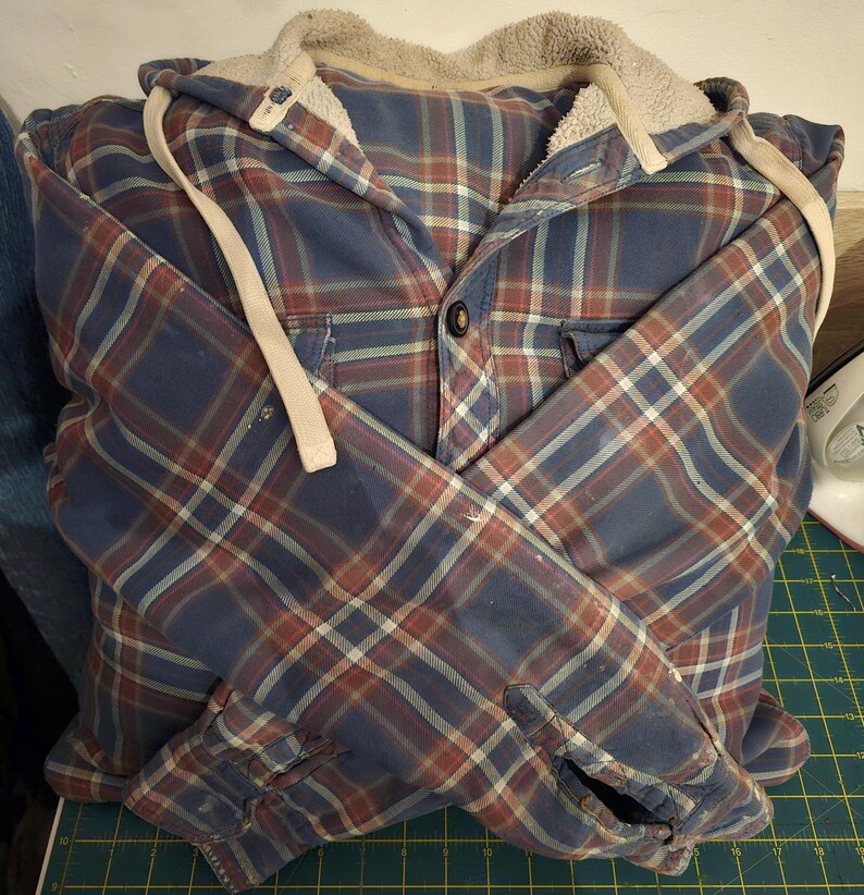 Puede incluir: Una camisa de franela a cuadros azules y rojos con capucha forrada de polar. Las mangas est&aacute;n remangadas y la camisa est&aacute; doblada por la mitad.