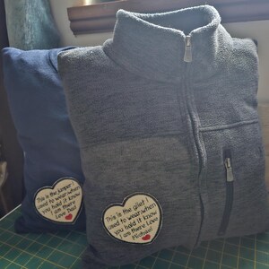 Puede incluir: Dos prendas de punto de polar gris con parches en forma de coraz&oacute;n cosidos. Los parches tienen texto bordado que dice "This is the jumper I used to wear when you hold it know I am there Love Dad" y "This is the gilet I used to wear when you hold it know I am there Love Michael".