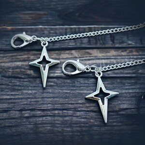 May include: Two silver star-shaped charms attached to a silver chain. The charms have a hollow center and are connected to a silver lobster clasp.