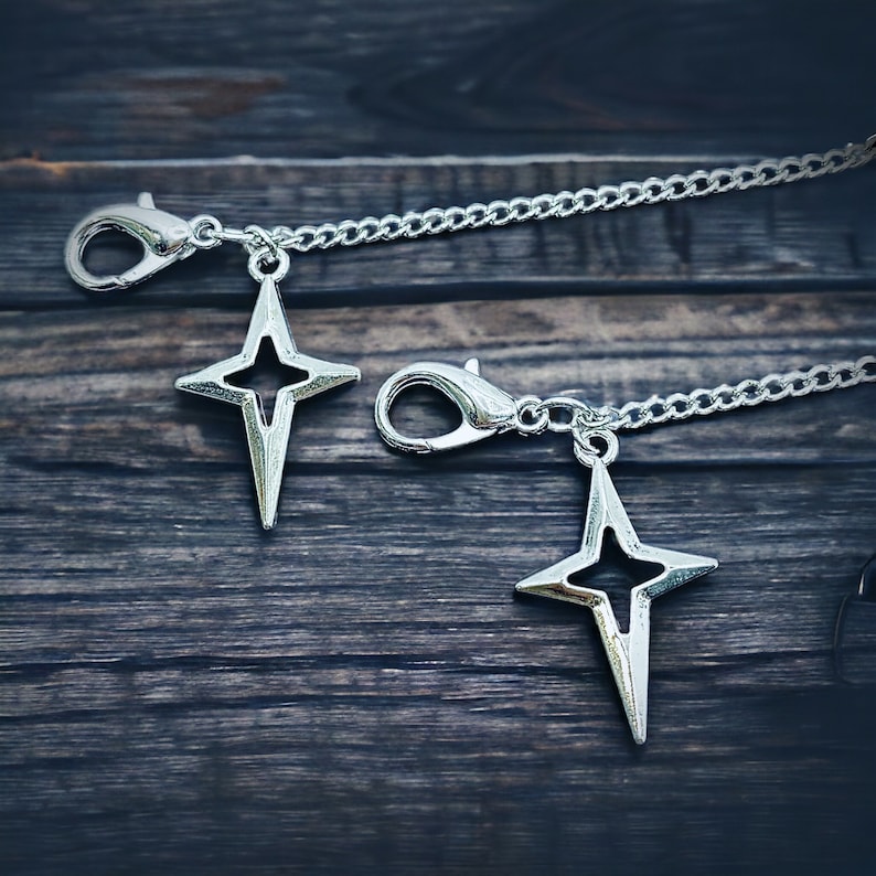 May include: Two silver star-shaped charms attached to a silver chain. The charms have a hollow center and are connected to a silver lobster clasp.