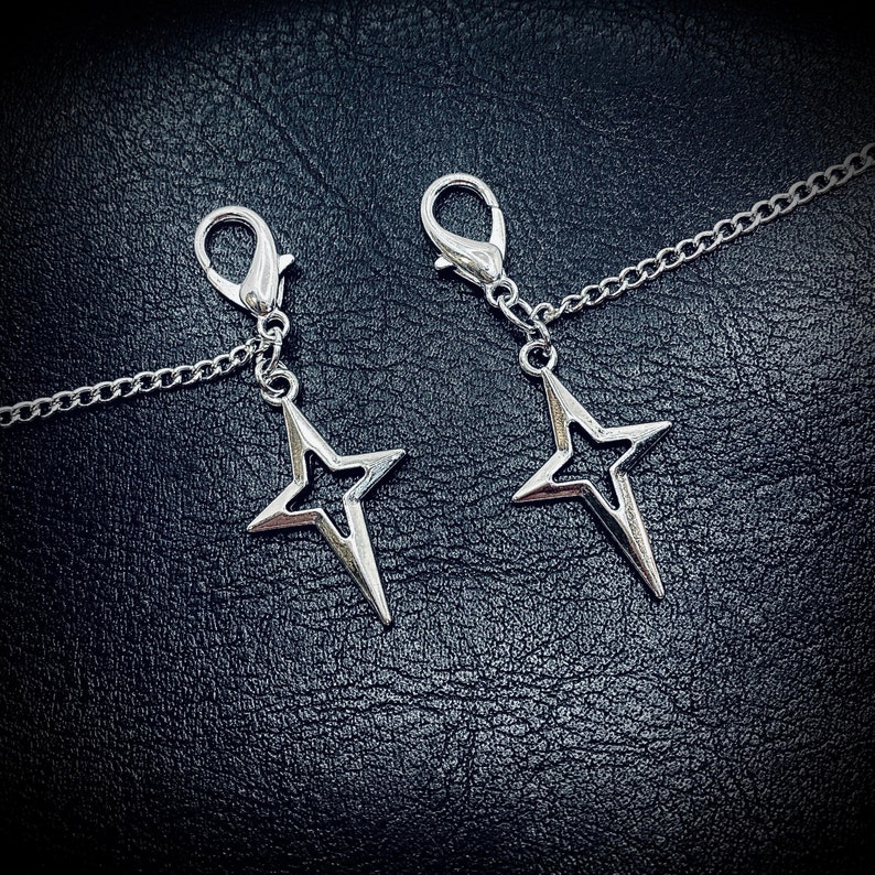 May include: Two silver star-shaped charms attached to a silver chain. The charms are open and have a delicate design.