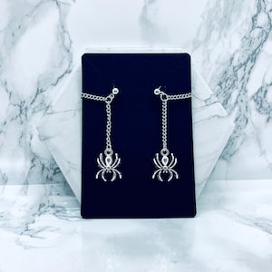 May include: A pair of silver spider earrings with dangling chains. The spiders are detailed and have a realistic appearance.