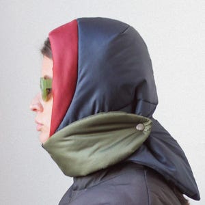 Puede incluir: Chaqueta y capucha acolchadas de color gris oscuro con diseño de bloques de color. La capucha presenta paneles rojos, azules y verde oliva. La chaqueta es de estilo abullonado y acolchado, ofreciendo calidez y estética moderna.