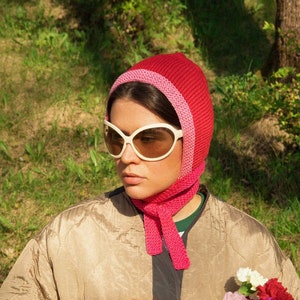 Puede incluir: Una persona con un gorro de punto rosa y blanco y gafas de sol sostiene una regadera amarilla llena de un ramo de flores rosas, amarillas y blancas.