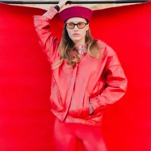 May include: A person wearing a red jacket, leggings, and a beret. The jacket has a zipper closure and pockets. The beret and leggings are a matching shade of red. The person is also wearing glasses.