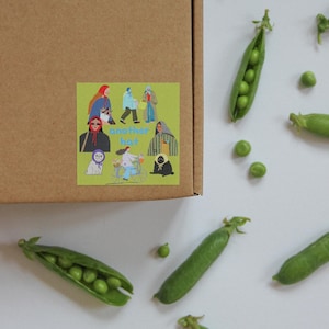 May include: A brown cardboard box with a sticker featuring illustrations of people and the text "another hat." Scattered around are fresh green pea pods and loose peas on a white surface.