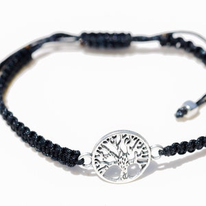 Puede incluir: Un brazalete trenzado negro con un dije de plata de árbol de la vida. El brazalete es ajustable con un nudo deslizante.