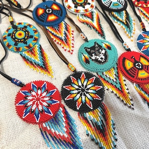 Op de afbeelding: Een verzameling van kralen Native American dreamcatchers met kleurrijke geometrische patronen en franjes. De dreamcatchers zijn gemaakt met zwarte leren koorden en hebben verschillende kleuren, waaronder rood, blauw, geel, wit en zwart.