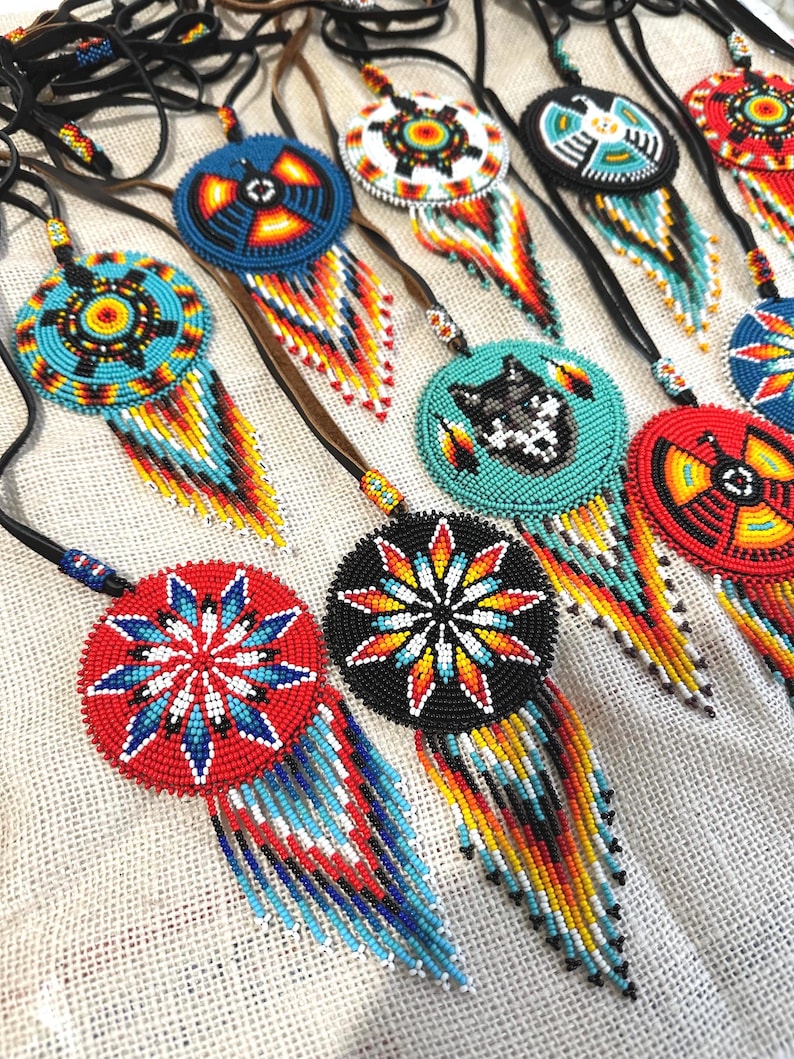 Op de afbeelding: Een verzameling van kralen Native American dreamcatchers met kleurrijke geometrische patronen en franjes. De dreamcatchers zijn gemaakt met zwarte leren koorden en hebben verschillende kleuren, waaronder rood, blauw, geel, wit en zwart.