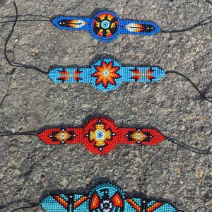 May include: Four beaded bracelets with colorful geometric patterns and a central circular design. The bracelets are blue, red, turquoise, and blue with black, white, and orange accents.