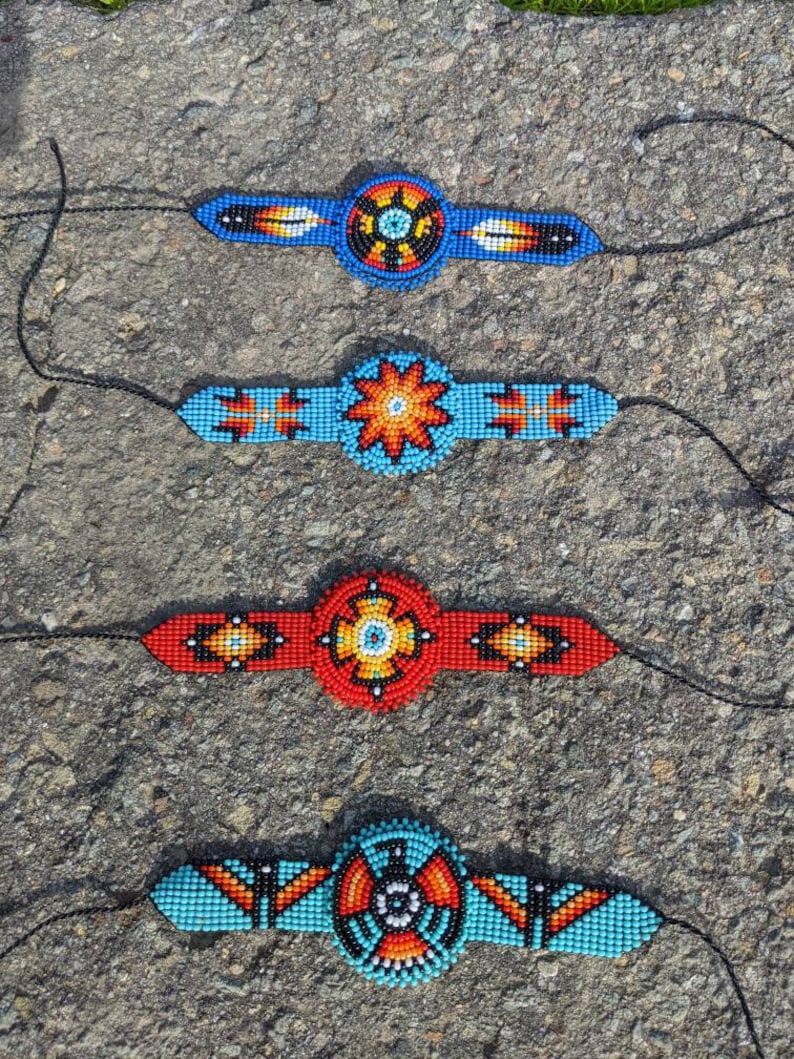 May include: Four beaded bracelets with colorful geometric patterns and a central circular design. The bracelets are blue, red, turquoise, and blue with black, white, and orange accents.