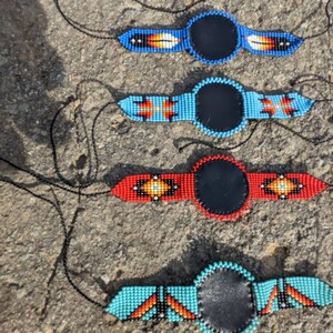 May include: Four beaded necklaces with leather circles in the center. The necklaces are blue, turquoise, red, and orange with geometric patterns.