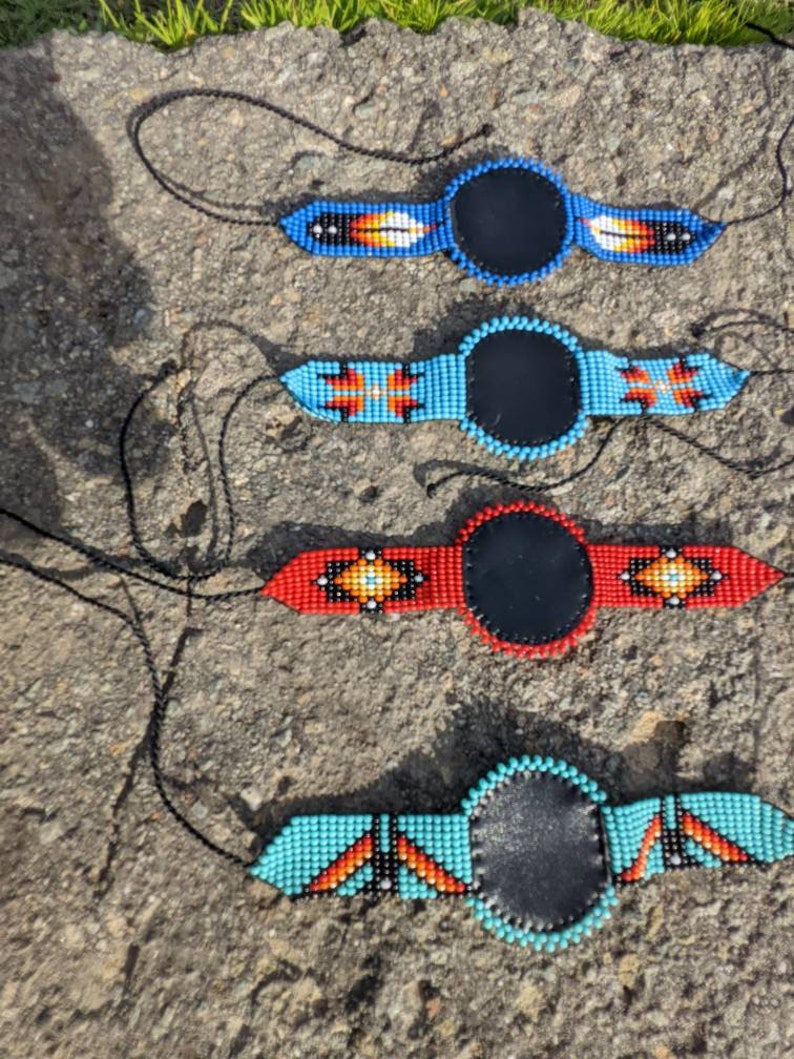 May include: Four beaded necklaces with leather circles in the center. The necklaces are blue, turquoise, red, and orange with geometric patterns.
