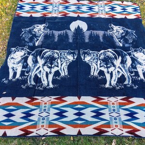 May include: A blue and white woven blanket with a pattern of wolves howling at the moon. The blanket has a geometric pattern of red, orange, blue, and white along the bottom edge.