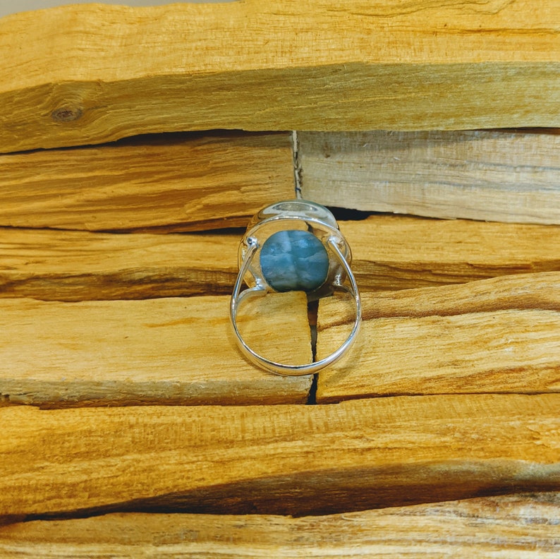 May include: A silver ring with a blue-green gemstone set in a bezel setting. The ring is on a wooden surface.