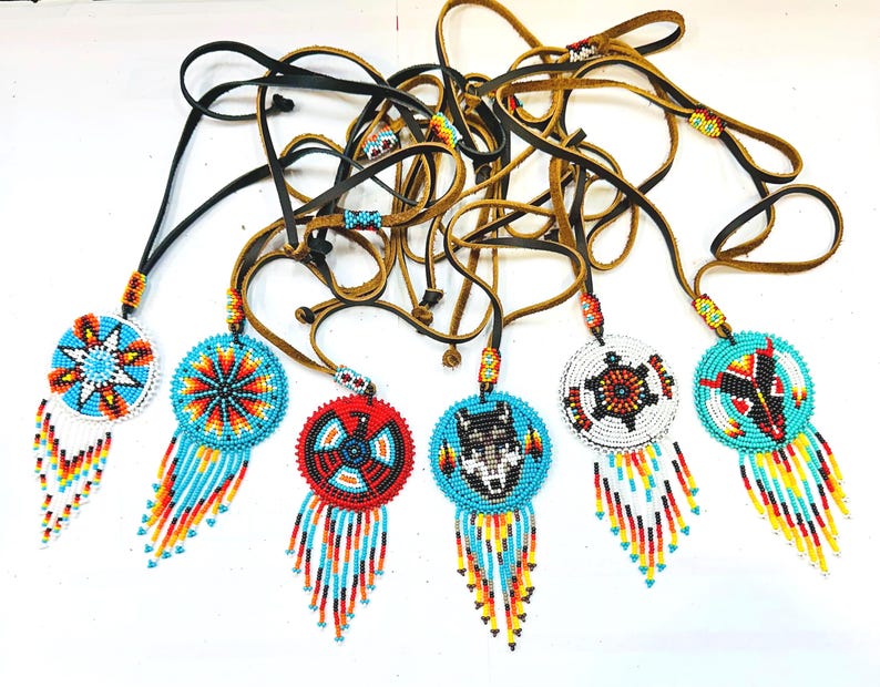 May include: Seven beaded necklaces with colourful, geometric patterns and fringe. Each necklace features a different design, including a star, a wolf, a turtle, and a bird. The necklaces are made with leather cords and beads in shades of blue, red, white, and yellow.