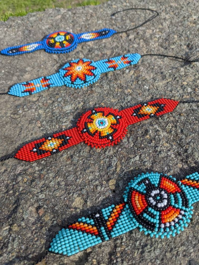 May include: Four beaded bracelets with colorful geometric patterns. Each bracelet features a central circular design with a variety of colors, including red, blue, orange, yellow, black, and white.