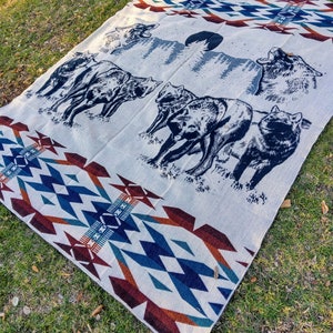 May include: A white woven blanket with a blue, red, and brown geometric pattern. The blanket features a scene of wolves howling at the moon in a forest.