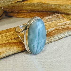 May include: A silver ring featuring a light blue oval-shaped gemstone. The gemstone has white streaks throughout.