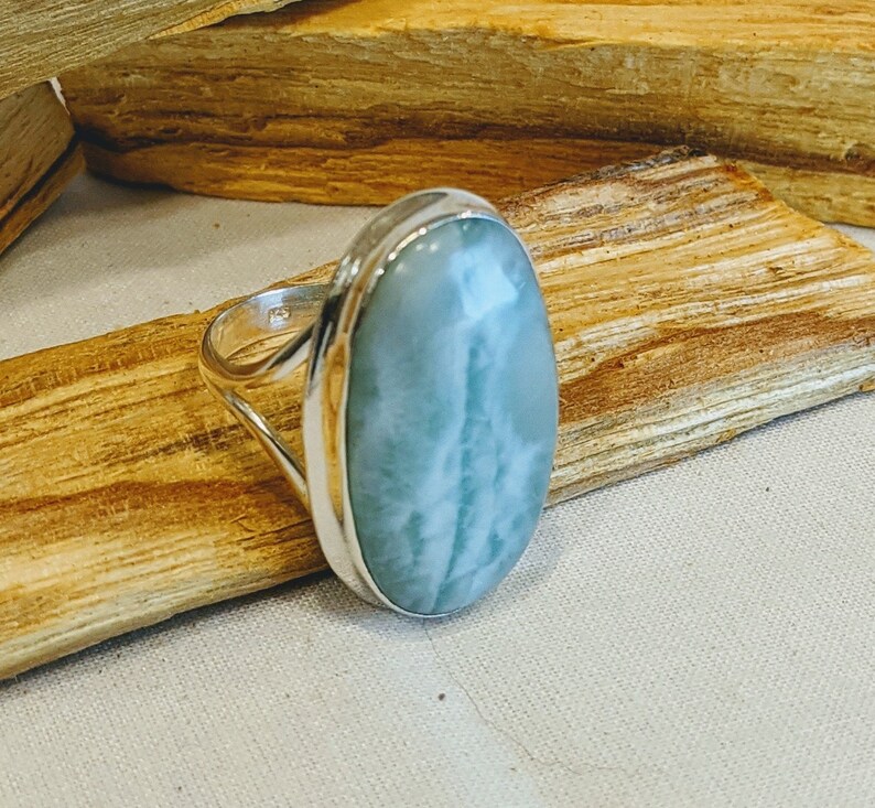 May include: A silver ring featuring a light blue oval-shaped gemstone. The gemstone has white streaks throughout.