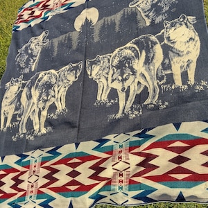 May include: A blue and white woven blanket with a pattern of red and white triangles. The blanket features a scene of wolves howling at the moon in a forest.