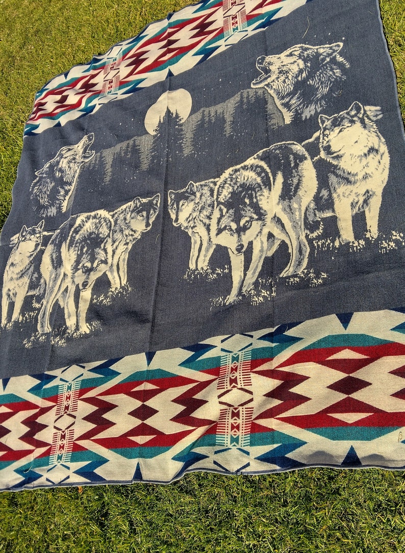 May include: A blue and white woven blanket with a pattern of red and white triangles. The blanket features a scene of wolves howling at the moon in a forest.