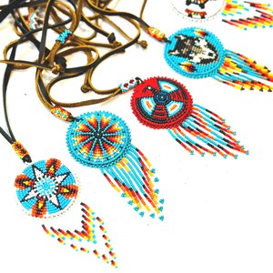 May include: A collection of beaded necklaces with colourful, geometric designs. Each necklace features a round pendant with a different pattern, including a star, a wolf, and a circle. The pendants are attached to leather cords.