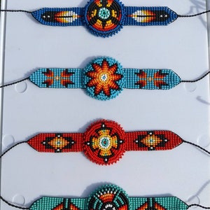 May include: Four beaded bracelets with colorful geometric patterns and round centerpieces. The bracelets are made with blue, red, orange, turquoise, black, and white beads.