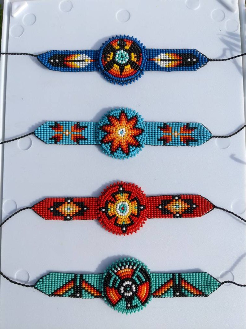 May include: Four beaded bracelets with colorful geometric patterns and round centerpieces. The bracelets are made with blue, red, orange, turquoise, black, and white beads.