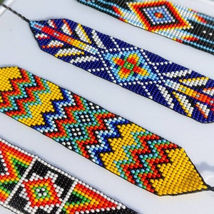 May include: Four colorful beaded bracelets with geometric patterns in shades of red, yellow, blue, green, white, and black.