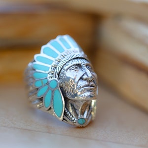 May include: A silver ring with a detailed design of an Native American chief wearing a headdress with turquoise stones.
