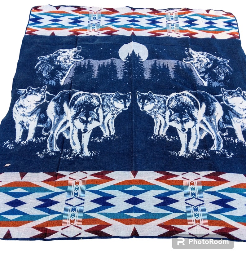 May include: A blue and white woven blanket with a pattern of triangles and diamonds. The blanket features a scene of wolves howling at the moon in a forest setting.