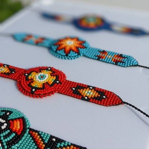 May include: Three beaded bracelets with colorful geometric patterns. The bracelets are made with small, colorful beads and feature a central circular design. The bracelets are displayed on a white surface.