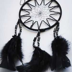 May include: Black dreamcatcher with black feathers and beads. The dreamcatcher has a circular frame with a web-like design in the center.
