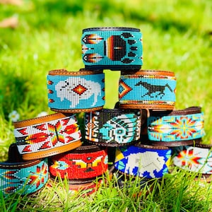 May include: A stack of colourful beaded leather bracelets with various Native American inspired designs, including a buffalo, a horse, and a bear paw print.