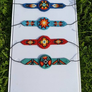 May include: Four beaded bracelets with colorful geometric patterns and a central circular design. The bracelets are displayed on a white background.