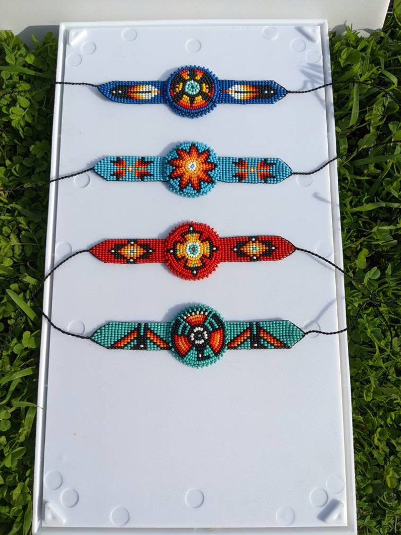 May include: Four beaded bracelets with colorful geometric patterns and a central circular design. The bracelets are displayed on a white background.