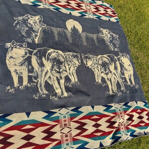 May include: A blue and white woven blanket with a pattern of red and white diamonds. The blanket features a scene of wolves howling at the moon in a forest.