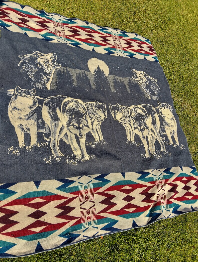 May include: A blue and white woven blanket with a pattern of red and white diamonds. The blanket features a scene of wolves howling at the moon in a forest.