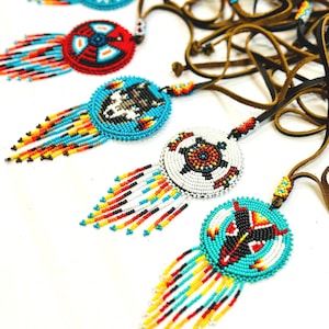 May include: A collection of beaded necklaces with colourful fringe. Each necklace features a round pendant with a different design, including a wolf, a turtle, and a geometric pattern. The necklaces are made with brown leather cords.