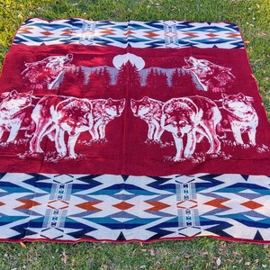 May include: Red and white patterned throw blanket with a design of wolves howling at the moon. The blanket features a geometric pattern in shades of blue, white, and orange.