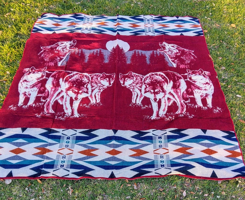 May include: Red and white patterned throw blanket with a design of wolves howling at the moon. The blanket features a geometric pattern in shades of blue, white, and orange.