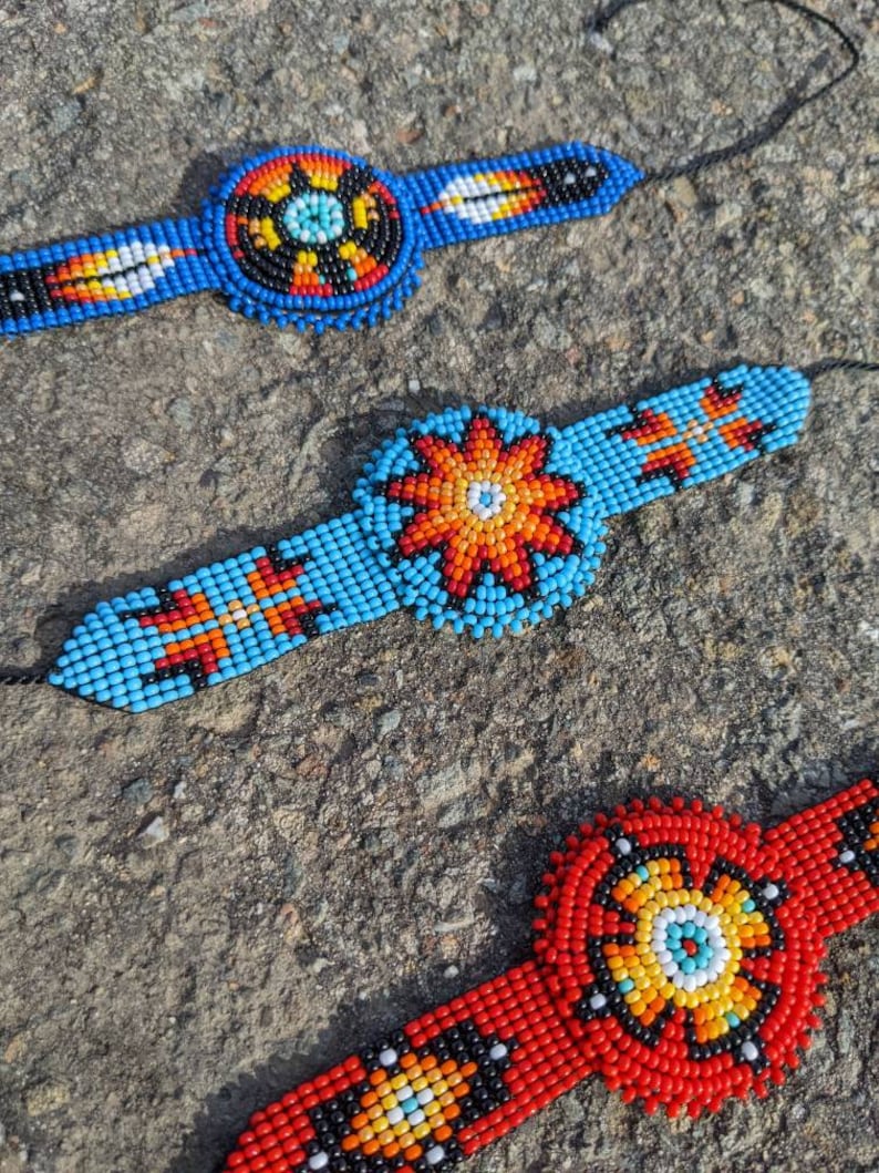 May include: Three beaded bracelets with colorful geometric patterns. The bracelets are made with blue, red, orange, yellow, white, and black beads. The center of each bracelet features a circular design.