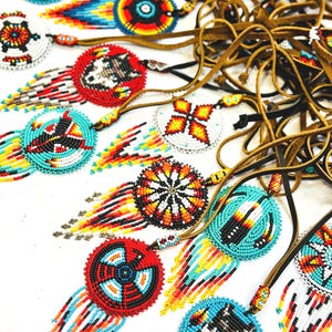 May include: A collection of beaded necklaces featuring colourful geometric patterns and fringe. The necklaces are made with turquoise, red, yellow, black and white beads.